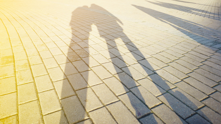 Shadows and silhouettes of people on paving stone at a city during sunset. Blank backgroundの写真素材