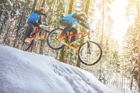 Collage of a two silhouettes of a cyclist in a jump. Mountain biking on trails in a snowy forest. Extreme winter sport. Bike rider flies through the air. Blur in motion abstract backgroundの写真素材