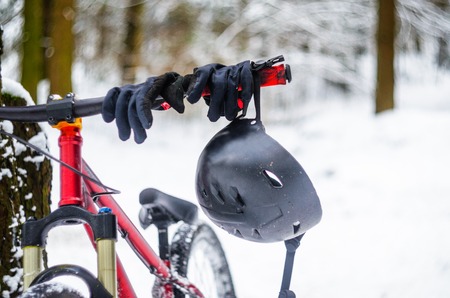 Black helmet with black sport gloves hangs on the handlebars of a bicycle in snowy winter forest. Mountain bike safety concept. Extreme sport backgroundの写真素材