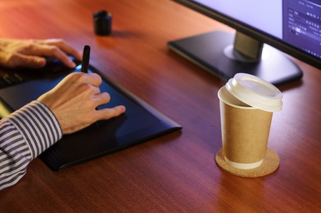 Desktop side view. Computer Graphics Tablet Cup of coffee Hand. Concept for website banner, mockup, background, presentation and marketing materialの写真素材