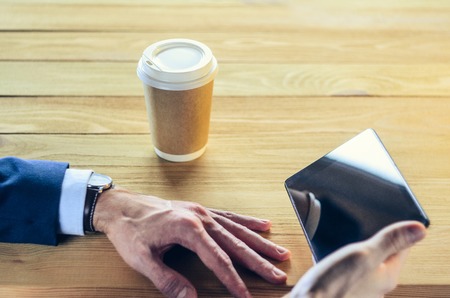 Businessman at a table in a cafe. Cup of coffee Tablet Blazer Hands Wooden table. Coffee Break Conceptの写真素材