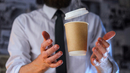 Barista, a bearded young man in a white shirt with a tie trying to catch a paper cup with hot coffee. Background for advertising. Empty place to your logo placementの写真素材