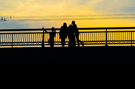 Silhouettes a Group of People on the High Bridge on a Background of Yellow Sunsetの写真素材