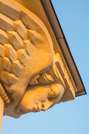 Stucco Sculpture of a Female Mask with Wings as a Decorative Element of the Building Against Blue...