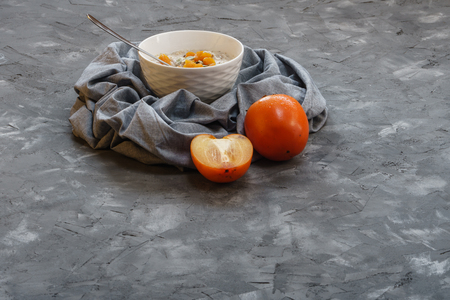 Oatmeal with Persimmon and Pumpkin Seeds on a Gray Rough Decorative Surface Top View. Copy Spaceの写真素材