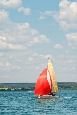 A small pleasure sailing yacht with scarlet sails goes to the bay on a sleepy day against the...