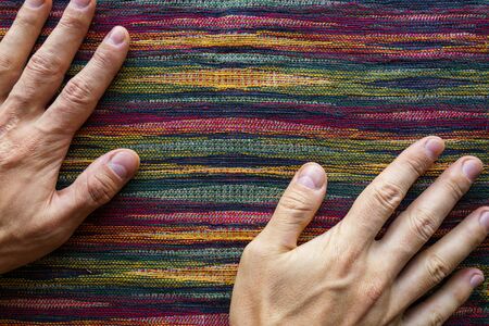 Man hands on motley striped fabric cloth material closeup. Tapestry background top viewの写真素材