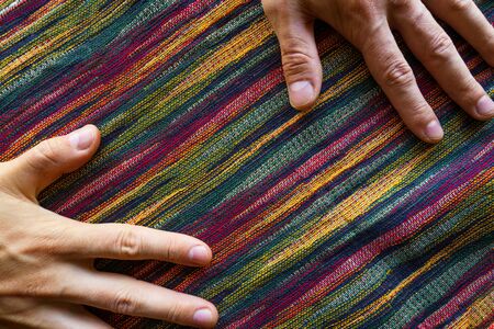 Man hands on motley striped fabric cloth material closeup. Tapestry background top viewの写真素材