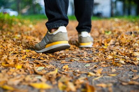 Walk on pavement in Autumn. Back view on the feet of a man walking along the pavement with fallen...