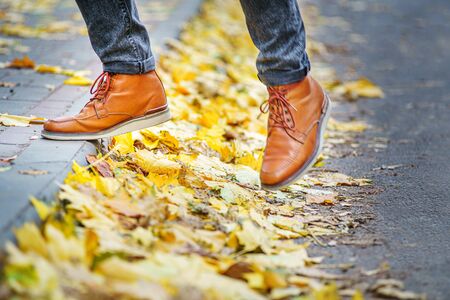 legs of a man in brown boots walking along the sidewalk strewn with fallen leaves. The concept of turnover of the seasons of the year. Weather backgroundの写真素材