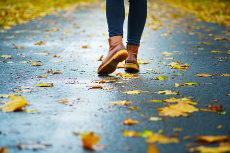 Walk on wet sidewalk. Back view on the feet of a woman walking along the asphalt pavement with puddles in the rain. Pair of shoe on slippery road in the fall. Abstract empty blank of the autumn weatheの写真素材