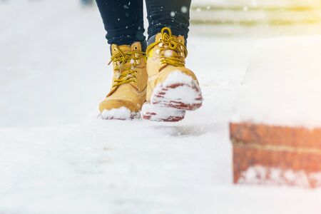 A woman in yellow leather shoes is walking along a snowy pavement. Winter walk. Abstract winter weather backgroundの写真素材