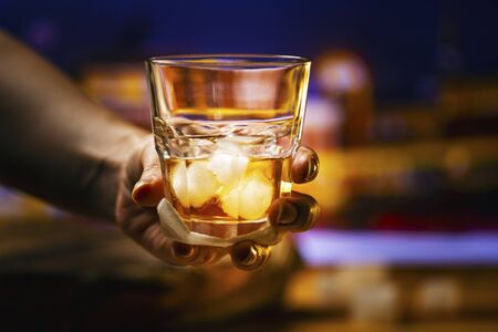 A glass of alcoholic beverage in hand. Whiskey cocktail with iceの写真素材