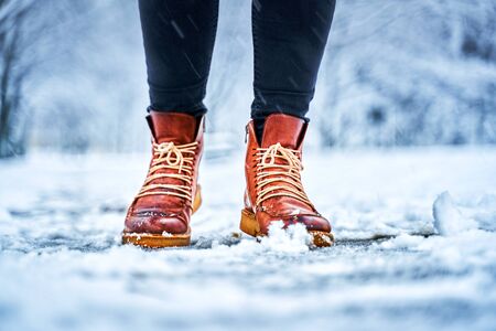 Feet of a woman on a snowy sidewalk in brown boots. Winter slippery pawement. Seasonal weather conceptの写真素材