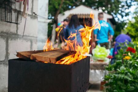 B-B-Q outdoors background. Kindling wood barbecue outdoors with open flame against the background of a group of peopleの写真素材