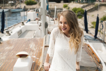 charming girl smiling while sitting on the wooden deck of a sailboatの写真素材