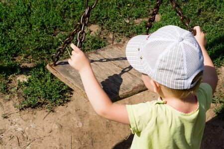A child who wants to swing on a wooden swing in the yardの写真素材
