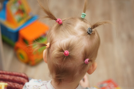 Hairstyle from numerous tails on the head of a little blonde girl. The first hairstyles the background of toysの写真素材