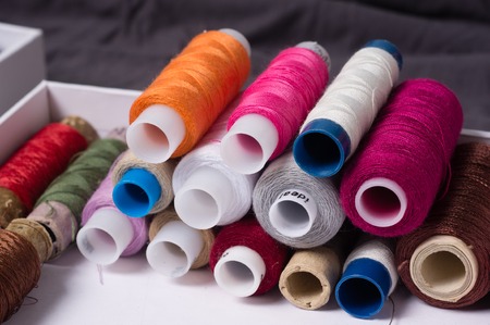 Various multicolored used sewing threads in a box, stacked in a pileの写真素材