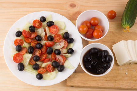 Greek salad with vegetables, feta cheese, black olives in process. Wooden background . Top viewの写真素材