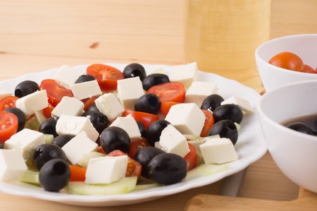 Greek salad with vegetables, feta cheese, black olives in process. Wooden background . Top viewの写真素材