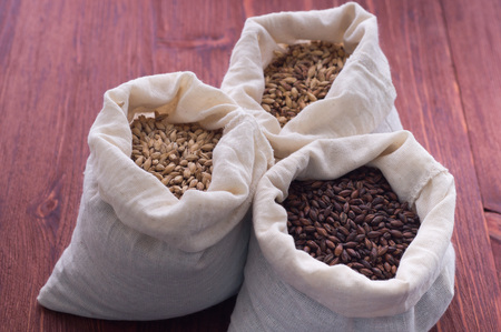 Pale, caramel, chocolate malt in a bags. Craft beer brewing from grain barley malt in process. Ale or lager from pale or dark pilsner malt. wooden backgroundの写真素材