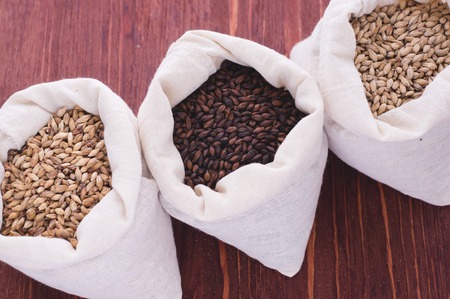 Pale, caramel, chocolate malt in a bags. Craft beer brewing from grain barley malt in process. Ale or lager from pale or dark pilsner malt. wooden backgroundの写真素材