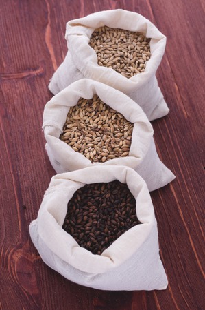 Pale, caramel, chocolate malt in a bags. Craft beer brewing from grain barley malt in process. Ale or lager from pale or dark pilsner malt. wooden backgroundの写真素材