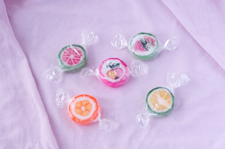 Colorful lollipops and different colored fruit round candy in wrapper on pink background
