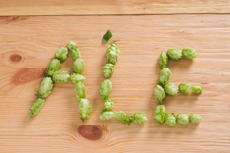 The inscription ale with hop cones on wooden background. Ingredient in beer industry. Craft beer brewing. For ale or lagerの写真素材
