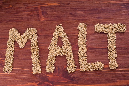 The inscription of malt by malt grains on wood background. Craft beer brewing from grain barley malt.の写真素材
