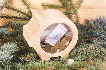 Yellow wooden piggy bank with russian ruble coins and banknotes. Christmas and New Year's wooden...