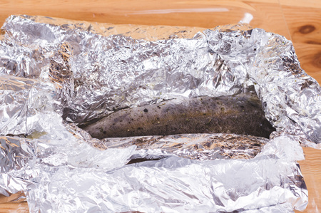 Tasty baked fish in foil at glass tray on wooden table. Healthy eating conceptの写真素材