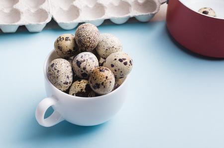Quail eggs in cup, red saucepan and cardboard packaging on blue background.
Vegetarian organic food. Eco products cocept.の写真素材