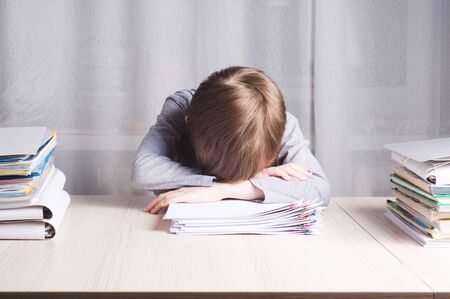 Tired school boy lying on the table clutching his head from too much workの写真素材