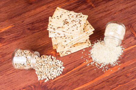 Stack of crispy wheat cakes with sesame seeds, flax and sunflower on a red wooden background and sunflower and sesame seeds in a jar. vegetarian food, eco food conceptsの写真素材