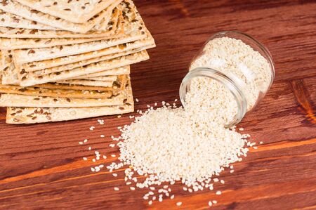Stack of crispy wheat cakes with sesame seeds, flax and sunflower on a red wooden background and sesame seeds in a jar.の写真素材