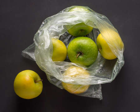 Transparent plastic crumpled cellophane bag with group of ripe green and yellow apples on a black...