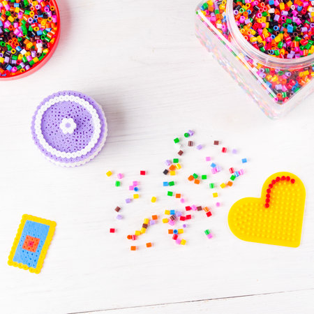 Thermomosaic beads in jar, heart-shaped form and crafts made from beads. Concept of quiet family game with children at homeの写真素材
