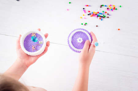 kids hands holding a homemade plastic jewelry box and thermomosaic beads on white background