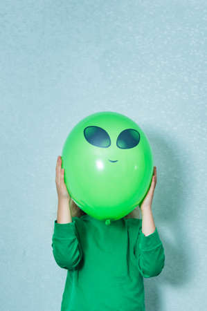 child dressed in green clothes playing alien. girl with a green ball where eyes and faces are drawn