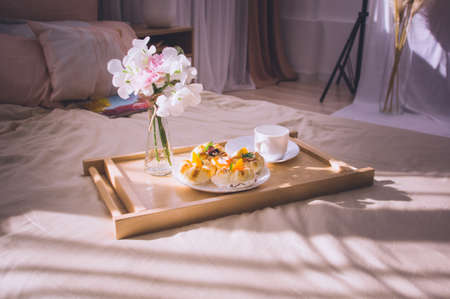 Soft blanket and tray with breakfast on bed indoors. Breakfast in bed. Window lightの写真素材