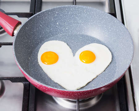 romantic breakfast - scrambled eggs in the form of a heart on a red frying pan on a stoveの写真素材