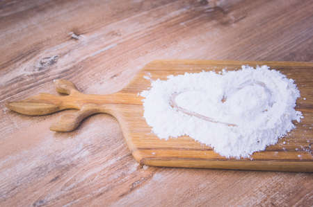 sprinkled wheat flour with a painted heart on a wooden board and wooden tableの写真素材