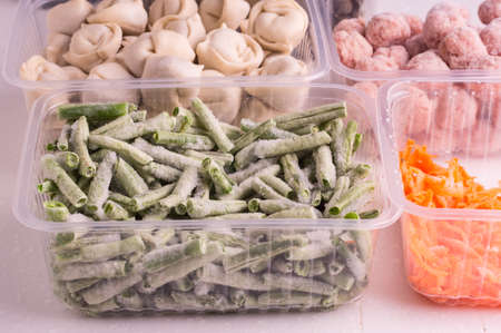 Frozen vegetables and semi-finished meat products in plastic containers on a white plate. meatballs, dumplings, chopped beans and grated carrotsの写真素材