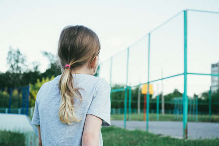 fair-haired girl in a gray t-shirt, looks at the school basketball court. back viewの写真素材
