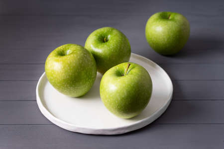 green apples on flat white handmade plate on a gray wooden tableの写真素材