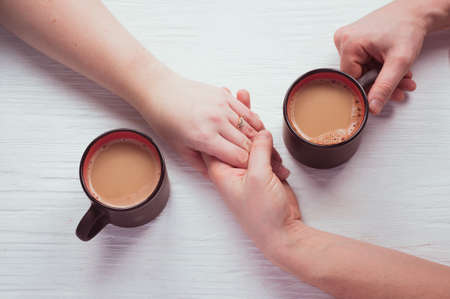 cups of coffee and holding hands of couple in love on white wooden table. Concept romantic date on Valentine's day. top view, flat layの写真素材