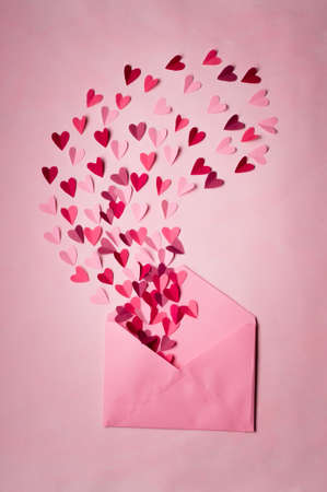 envelope with paper hearts on a pink background. Hearts take off from inside open envelope. Romantic...