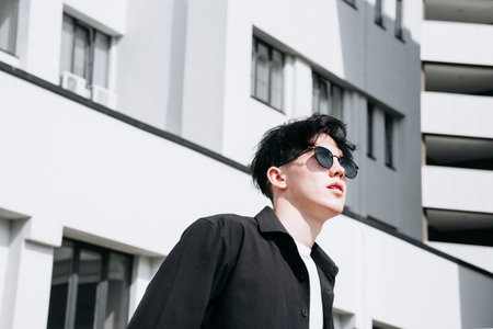 handsome young man in a black shirt standing against the backdrop of city buildings and looking away...